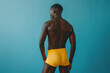 © Augustino - Male underwear concept. Studio shot of back of sportive afro-american athlete wearing yellow swimming briefs and isolated on blue background. Copy-space