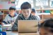 © spyrakot - Focused Chinese Schoolboy Working on Laptop in Modern, Brightly Lit Classroom with Classmates