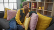 © Krakenimages.com - A relaxed bearded redhead man lounging on a grey sofa indoors with colorful pillows and a bookshelf.