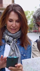 Wall Mural - Happy senior adult tourist couple holding city map while enjoying a walk in Barcelona. Married middle aged man and woman looking for touristic location on phone app during vacation. Vertical HD video