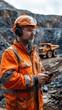 © BoOm - A construction worker in an orange safety suit and helmet, using a tablet on a mining site, surrounded by towering rock formations.