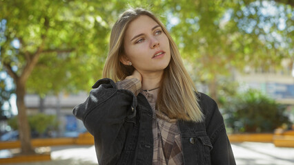 Poster - A young caucasian woman with blonde hair outdoors, surrounded by nature, looking pensive in a park setting.