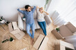 © Prostock-studio - A young couple rests on a sofa in their new home, surrounded by moving boxes.