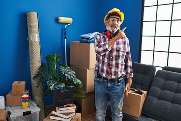 Wall Mural - Cheerful senior man in hardhat, safety glasses points happily to the side in his new home with a natural smile