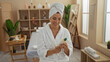 © Krakenimages.com - Woman smiling in a spa wearing a bathrobe and towel while holding a lotion bottle in a serene wellness center setting.