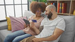 © Krakenimages.com - An interracial couple lounging on a sofa, happily shopping online with a credit card and tablet in a cozy home setting.