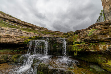 Picturesque waterfall flowing over layered rock formations with lush green moss in Cantabria, Spain. Ideal for nature, travel, and landscape themes.