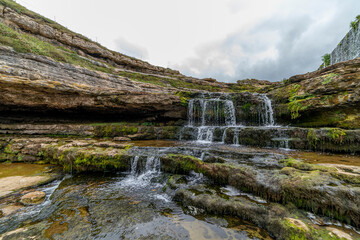 Picturesque waterfall flowing over layered rock formations with lush green moss in Cantabria, Spain. Ideal for nature, travel, and landscape themes.