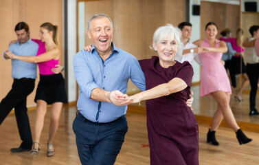 Wall Mural - Cheerful elderly couple practicing ballroom dances in ballroom