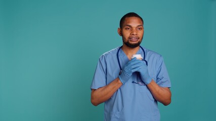 Happy male nurse enjoying fresh cup of coffee during job shift break. Cheerful healthcare specialist isolated over studio background drinking hot beverage while at work, camera B