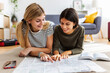 © Xavier Lorenzo - Two young female friends looking at map while planning their next summer trip at home. Travel and vacation lifestyle concept.
