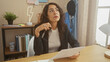 © Krakenimages.com - A thoughtful middle-aged hispanic woman in a blazer holds glasses at a home office desk, pondering documents.