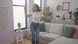 © Krakenimages.com - A happy woman dances in a cozy living room with modern decor, plants, and a lavender wall.