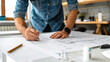 © sommersby - A person sketches architectural plans on a large sheet of paper at a well-lit workspace