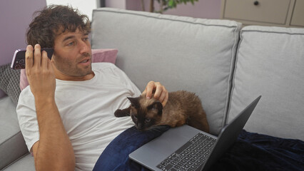 Poster - A young hispanic man listens to a voice message while relaxing on a couch in his living room with a cat on his lap and a laptop nearby.