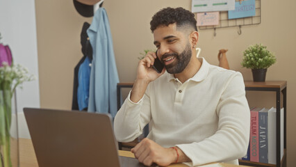 Sticker - A bearded young man talks on the phone in a cozy apartment interior while working on a laptop