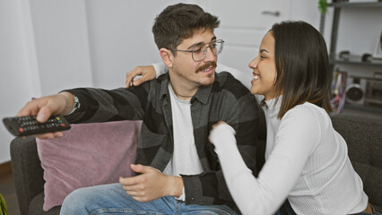 Wall Mural - Happy couple enjoying a cozy moment together on the sofa in a modern living room, man holding remote.