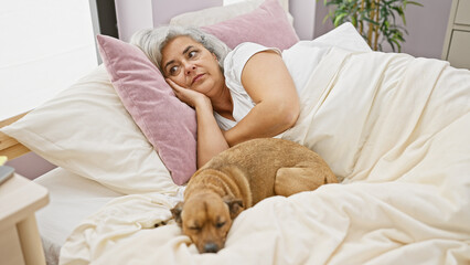 Wall Mural - A contemplative elderly woman lies in bed with her resting dog in a cozy bedroom setting.