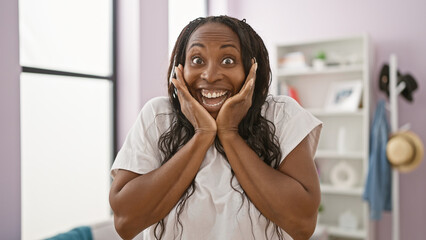 Canvas Print - Excited african american woman with curly hair smiling indoors against a living room background