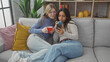 © Krakenimages.com - Two women enjoying coffee while browsing a smartphone together on a cozy living room couch.