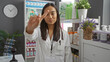 © Krakenimages.com - Young woman in pharmacy shop gesturing no with finger while wearing white coat among shelves of products