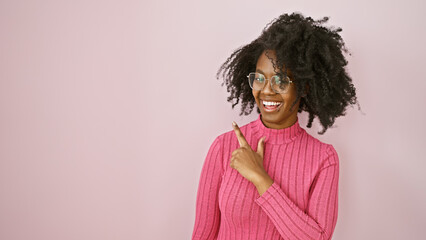 portrait of a smiling african american woman in glasses on a pink background pointing to empty space