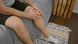 © Krakenimages.com - Young caucasian man in shorts sitting indoors holding his knee as if experiencing pain or discomfort.