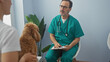 © Krakenimages.com - A hispanic man in veterinary scrubs consults a tablet in a clinic, facing a poodle and its owner.