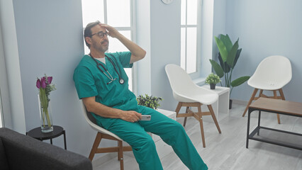 Sticker - A middle-aged male doctor in scrubs looks exhausted in a modern hospital waiting room