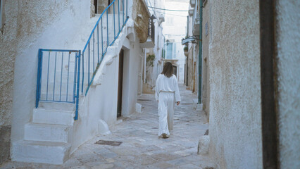 Wall Mural - A young hispanic woman walks through the beautiful, narrow streets of polignano a mare in puglia, italy, surrounded by whitewashed buildings and rustic charm.