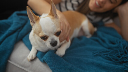 Canvas Print - A young woman relaxes at home, gently touching her pet chihuahua on a couch with a blue blanket.