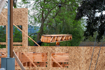Wall Mural - Residential house construction, boom crane lifting lumber delivery, wood support truss beams, workman assisting in placement
