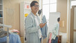 © Krakenimages.com - A smiling young asian man holding a smartphone stands in a modern wardrobe room surrounded by casual clothing.