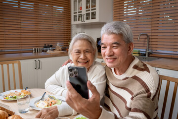 Asian senior couple using phone video call while having dinner in house.