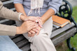 © bongkarn - A close-up image of a caring daughter holding her mom's hand while talking, both sitting on a bench.