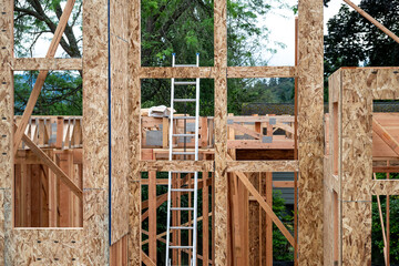 Wall Mural - New house construction in residential neighborhood, first floor framed and exterior wall OSB sheeting installed, aluminum extension ladder propped up inside, sunny summer day on job site
