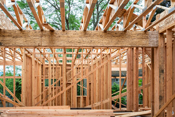 Wall Mural - New house construction in residential neighborhood, job site detail, first floor interior wood framing installed, looking up at wood truss support beams for second floor, summer day on job site

