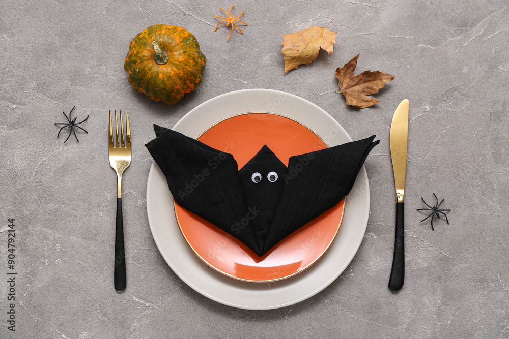 Festive table setting with napkin folded in shape of Halloween bat on grey grunge background