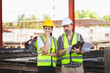 © JU.STOCKER - Cheerful engineer and female foreman worker with blueprints and digital tablet checking project at the precast concrete factory site, Engineer team in hardhats discussing on construction site
