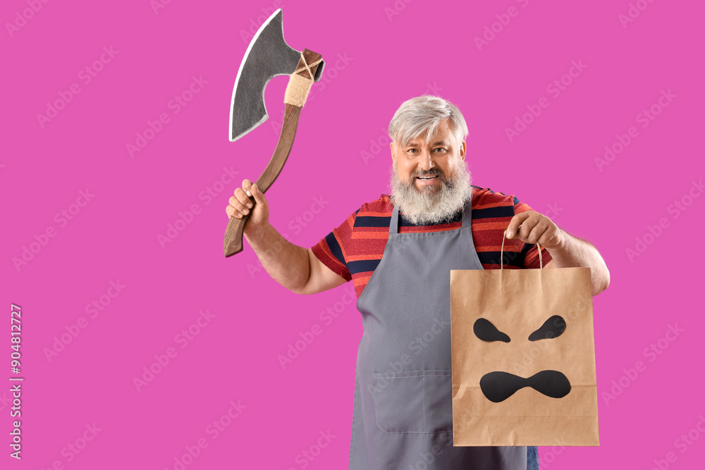 Mature man dressed for Halloween with axe and gift bag on pink background