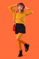 Poster - Stylish young woman in fall clothes on orange background