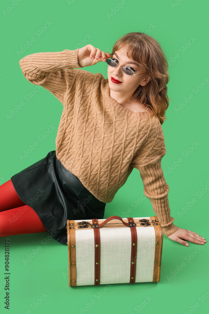 Stylish young woman in fall clothes sitting on green background