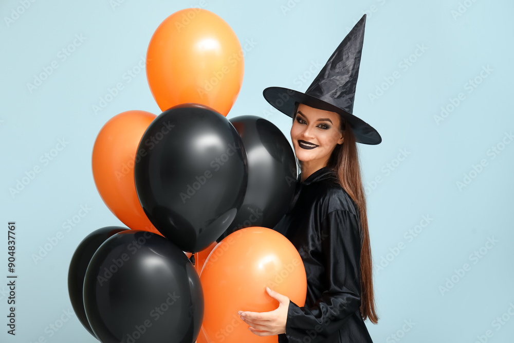 Young woman dressed for Halloween as witch with balloons on blue background