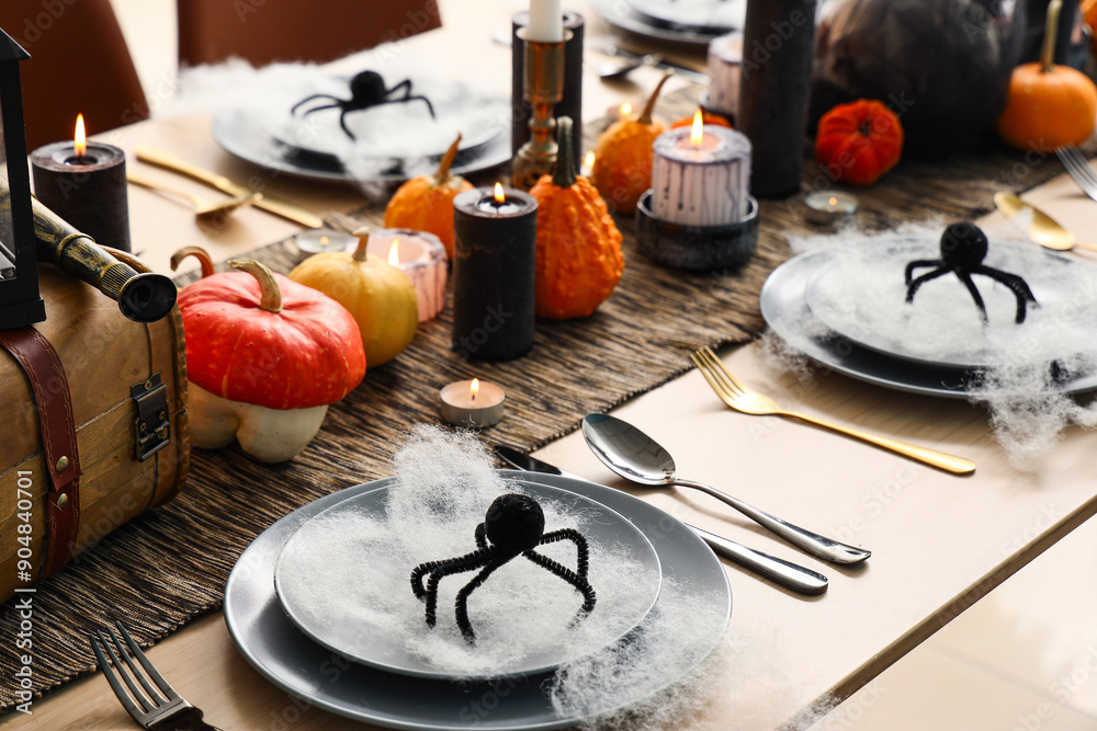 Festive table setting for Halloween party with burning candles, pumpkins, spiders and web, closeup