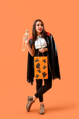 Poster - Young woman dressed for Halloween with gift bag and skeleton on orange background