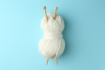 Poster - White yarn with knitting needles on light blue background, top view