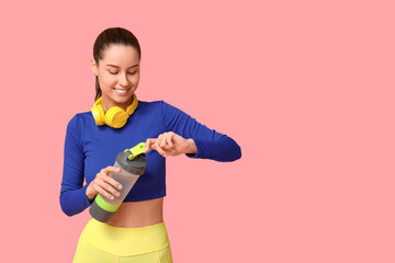 Poster - Young sporty woman in headphones with water bottle on pink background