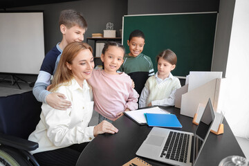 Wall Mural - Mature teacher in wheelchair with little pupils hugging during lesson at school