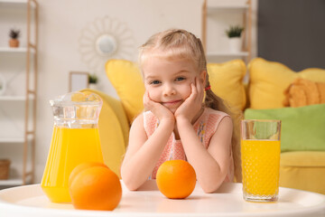 Wall Mural - Cute little girl with orange juice and fruits near table at home