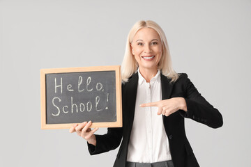 Sticker - Mature female teacher pointing at chalkboard with text HELLO SCHOOL on light background